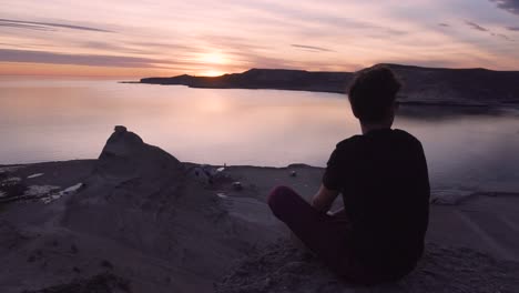 Young-Model-seated-on-top-of-a-mountain-watching-the-sunset---Wide-shot