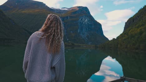 Blonde-girl-wearing-a-white-sweater,-observing-beautiful-scenic-view-of-a-large-lake-and-mountains-in-the-background