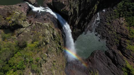 Beautiful-waterfall-cascading-over-rock,-rainbow-splashback-mist,-aerial-view