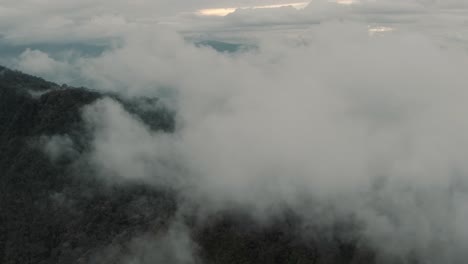 Drone-aerial-flying-high-through-the-clouds-over-mountain-and-forest