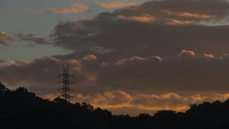 Morgens-Goldene-Wolken,-Die-Sich-Hinter-Dem-Berg-Und-Dem-Elektrischen-Turm-Bewegen