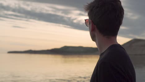 Young-Man-Wearing-Sunglasses-looking-At-the-Calm-Ocean-During-Sunset