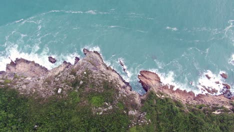 Aerial-view-of-a-jagged-rock-island,-surrounded-with-lush-green-nature-and-Hong-Kong-bay-water