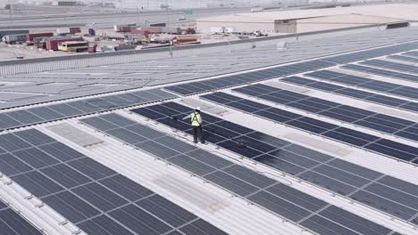 Man-With-Reflectorized-Vest-And-Safety-Helmet-Cleaning-Solar-Panels-On-Top-Of-A-Large-Industrial-Warehouse-In-Dubai,-United-Arab-Emirates
