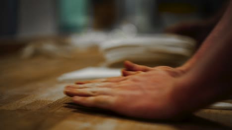 close-up-shallow-focus-shot-of-baker-shaping-triangle-slab-of-dough-into-a-croissant-by-rolling-it-tightly-with-both-hands-over-wooden-table