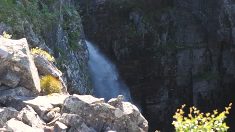High-angle-wide-shot-of-the-Njupeskärs-waterfall-Drop,-at-high-noon,-with-mosquitoes-flying-between-the-sunbeams,-at-Fulufjället-National-Park,-in-Sweden