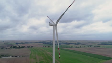 Lone-Tri-Blade-Windmill-Stop-Spinning-In-Greenfield-Against-A-Cloudy-Sky-In-Kwidzyn,-Poland---Drone-Shot