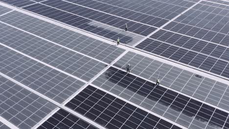 Men-At-Work-On-The-Roof-Of-A-Warehouse-Cleaning-Solar-Panels---ascending-drone-shot