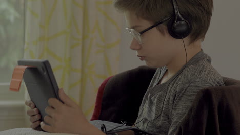 Closeup-of-a-young-boy-on-a-tablet-and-wearing-headphones-at-home-in-a-virtual-class