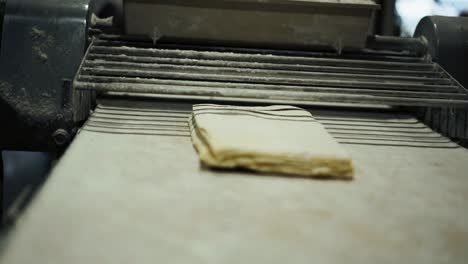 Medium-shot-of-slab-roller-croissant-dough-machine-rolling-sheets-of-laminated-croissant-dough,-focus-pulling-from-machine-to-pastry