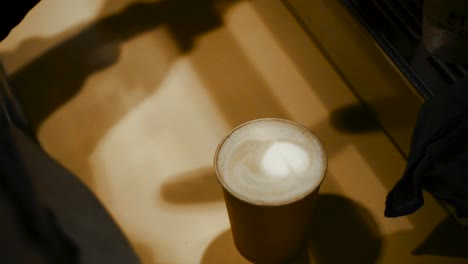 High-angle-detail-shot-of-barista-finishing-a-latte-with-heart-shaped-foam-in-the-center---slow-motion