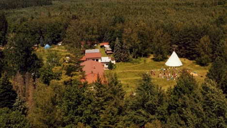 Drone-Aerial-flying-over-amazing-dense-green-forest-revealing-epic-event-center-with-massive-Teepee-and-Outdoor-Yoga-Class-taking-place
