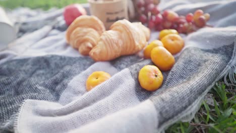Romantic-picnic-on-a-blanket-of-gray-with-apples,-grapes,-mandarins,-croissants-and-fruits-in-a-straw-bag-on-the-beach