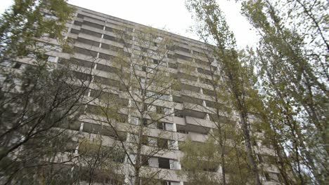 Mirando-Un-Viejo-Edificio-Abandonado-A-Través-De-árboles-En-Prypiat,-Chernobyl--inclínate-Hacia-Arriba