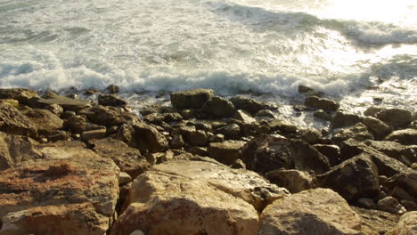 Waves-Crashing-on-the-Rocks-at-Shore,-Bright-Evening-Sun-Flare