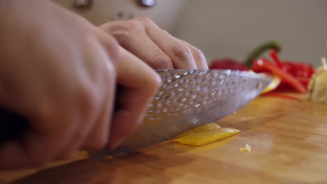 Close-up-on-steel-knife-slicing-yellow-color-pepper-on-wooden-cut-board