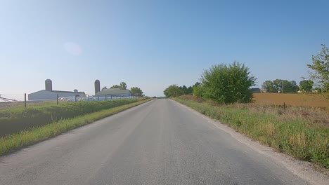 POV-while-driving-past-farmyards-and-field-on-a-country-road-in-rural-Iowa-in-late-summer