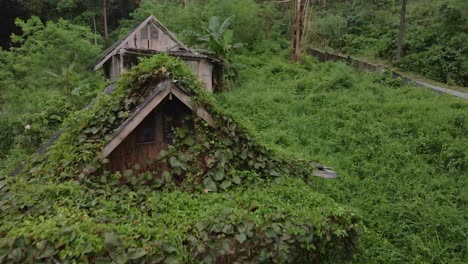 dolly-tilt-down-shot-drone-view-of-old-style-wooden-Thai-bungalow-that-is-now-taken-over-by-jungle,-derelict-and-unused-due-to-the-effects-of-the-pandemic-on-travel-and-tourism-in-South-east-asia