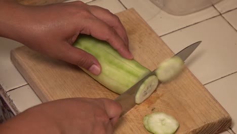 Hands-slicing-a-cucumber-on-a-cutting-board