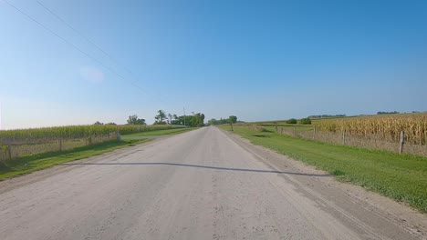 Pov-Während-Der-Fahrt-Vorbei-An-Feldern-Auf-Einer-Breiten-Schotterstraße-Im-Ländlichen-Iowa-Im-Spätsommer-Mit-Weitem-Blauem-Himmel