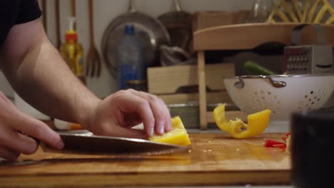 Chef-cuts-in-half-big-yellow-color-pepper-with-steel-knife-on-wooden-cut-board-on-a-kitchen-table
