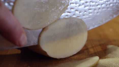 Extreme-close-up-on-slicing-fresh-potato-with-steel-knife-on-wooden-cut-board