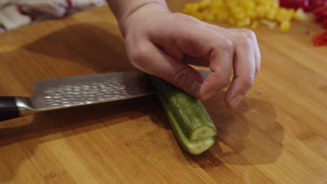 Close-up-on-steel-knife-slicing-green-cucumber-on-wooden-cut-board