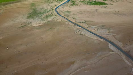 Aerial-overhead-view-of-a-winding-narrow-river-on-a-drought-area-debouching-into-a-lake