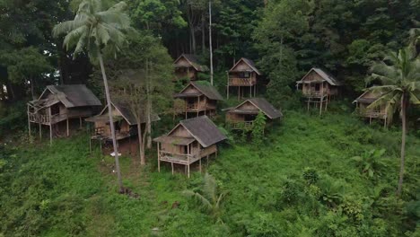 backwards-dolly-shot-drone,-aerial-birds-eye-view-of-old-backpacker-style-wooden-bungalows-in-South-east-Asia-that-are-now-derelict-and-unused-due-to-the-effects-of-the-pandemic-on-travel-and-tourism