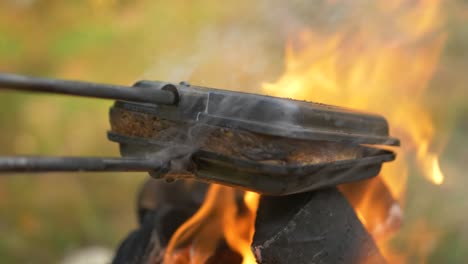 Close-up-shot-of-Square-sandwich-Pie-Iron-Cast,-grilling-cheese-Sandwich-over-hot-campfire