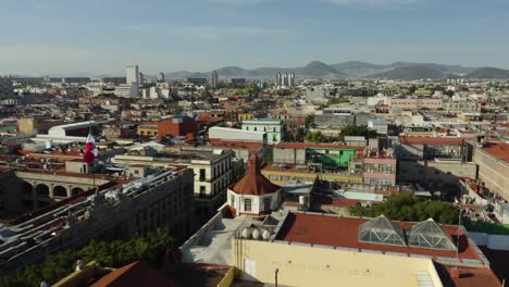 Aerial-Shot-of-Mexico-City,-Pedestal-Down-with-Mexican-Flag-Waving-in-the-Wind