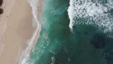 Top-down-aerial-view-of-tropical-beach-with-azure-blue,-turquoise-water-and-foaming-ocean-waves-crashing-on-wild-beach