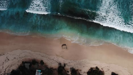 Aerial-view-of-waves-rolling-one-by-one-to-the-Nunggalan-Beach,-Uluwatu,-Bali,-Indonesia-|-Bali,-South-Kuta-top-view-of-the-picturesque-wrecked-ship