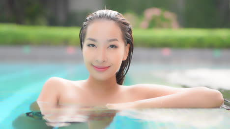 Happy-Sensual-Asian-Woman-Relaxing-in-Swimming-Pool,-Looking-Straight-to-Camera