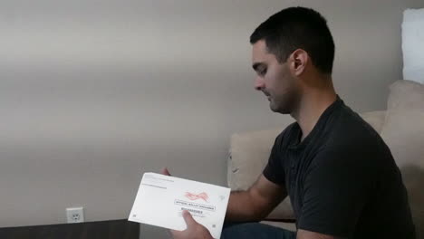 Young-Man-Opens-and-Reads-Official-Election-Mail-in-Ballot-on-Couch-in-Home