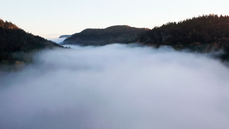 High-Aerial-Pan-Left-Above-Fog-in-Misty-Mountain-Valley-at-Sunrise