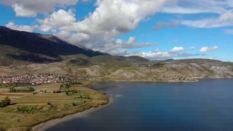 Pueblo-A-Orillas-Del-Lago-Prespa,-Montaña-De-Reflejo-De-Agua-Y-Nubes-En-Un-Paisaje-Relajante