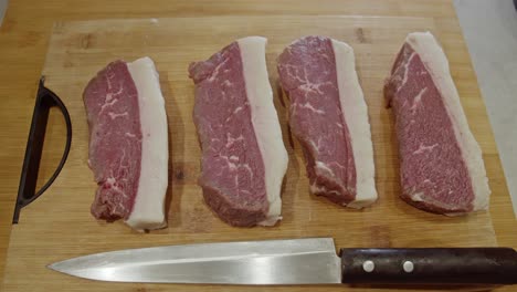 Four-meat-steaks-and-kitchen-knife-on-top-of-wooden-cut-board