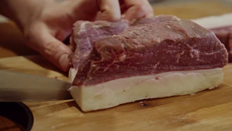 Slicing-the-steak-with-steel-kitchen-knife-against-the-nerve-on-wooden-cut-board