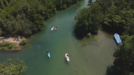 Aerial-drown-birds-eye-view-slow-moving-backwards-dolly-of-paddle-boarders-slowly-paddling-up-river-surrounded-by-tropical-jungle