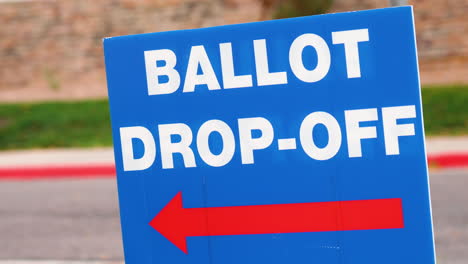 Blue-Ellection-Ballot-Drop-off-Sign-with-Red-Arrow-Pointing-Left-and-Blowing-in-the-Wind-Outside