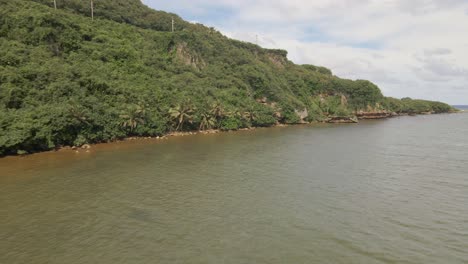 Drone-flying-low-over-the-water-near-cliffs-of-a-tropical-island