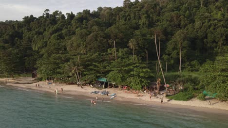 Tropical-Island-drone,-trucking,-rotating-shot-with-rain-forest-and-palm-trees-with-white-sand-beach,-kayaks-,small-beach-bars-with-some-Thai-domestic-tourists-enjoying-a-long-weekend