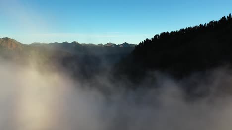 Frying-Through-Fog-Above-Valley-and-Evergreen-Forest-Under-Blue-Sky-and-Mountain-Peaks-on-Sunny-Morning
