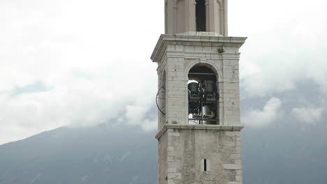 Close-up-handheld-shot-of-bells-tolling-in-a-church-tower-with-misty-mountains-in-background