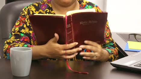 Black-woman-dressed-in-vintage-shirt-reading-bible-at-desk-at-work-in-office,-cup-of-coffee,-New-Normal