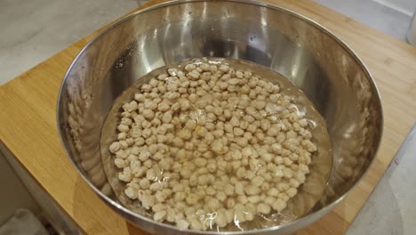 Chef-puts-a-metal-bowl-with-chickpeas-for-soaking-on-a-wooden-table-in-the-kitchen