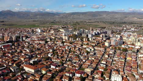 Suburban-area-of-Korca-city-in-Albania-with-red-roofs-and-buildings-surrounded-by-mountains