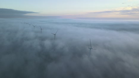 Side-panning-aerial-shot-of-windturbines-rotating-in-the-clouds-on-a-epic-sunrise-with-low-clouds