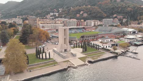 Monumento-De-Guerra-De-Piedra-En-Forma-De-Torre-Con-El-Estadio-Giuseppe-Sinigaglia-En-El-Fondo,-Como,-Lombardía,-Italia